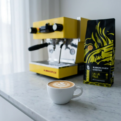Yellow espresso machine with a cup of coffee and a bag of Karon Farm Coffee on a marble surface.