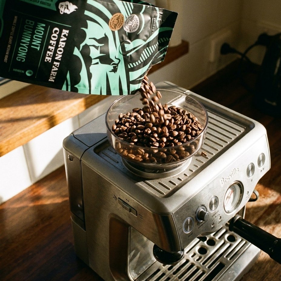 Espresso machine with beans being poured into a grinder from a Karon Farm Coffee coffee bag.