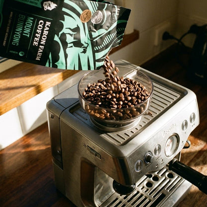 Espresso machine with beans being poured into a grinder from a Karon Farm Coffee coffee bag.